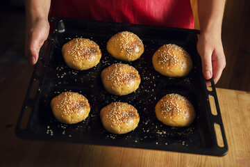 Delicious sesame buns in the hands of a girl. Freshly Baked Buns. Hamburger buns are hot, fresh...