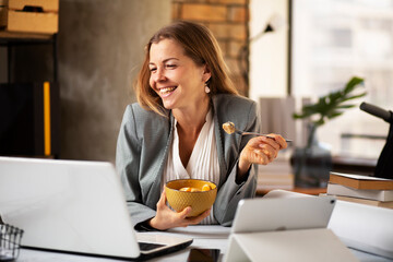 Businesswoman in office having healthy snack. Young woman eating fruit while having a video call.
