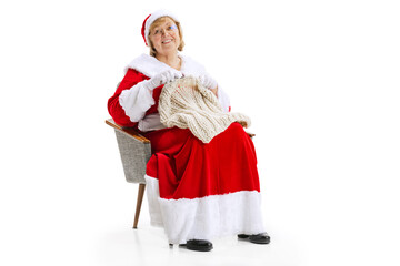 Portrait of happy smiling beautiful middle-age woman in Christmas costume sitting at armchair and knits sweater isolated on white background.