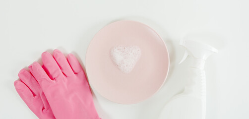 Dish washing concept. Pink gloves, heart shaped foam on plate and white spray bottle. White  background. Flat lay, copy space. Banner size
