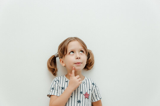 Little cute girl with big beautiful eyes. Studio shot, white background, minimalism. Emotion cunning, interest, thoughtfulness, mysteriousness, humor