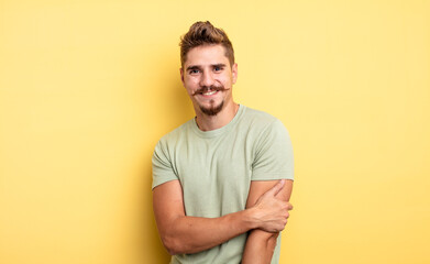 young handsome man laughing shyly and cheerfully, with a friendly and positive but insecure...