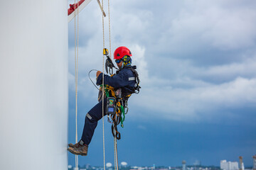 Close-up male workers control equipment rope down tank rope access background cloud storm.