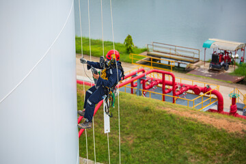 Male workers control rope down top roof tank rope access inspection of thickness shell plate storage tank gas