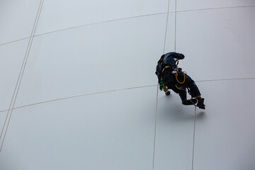 Male workers control rope down height tank rope access inspection of thickness shell plate storage tank.