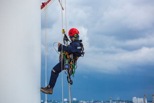 Close-up male workers control equipment rope down tank rope access background cloud storm.