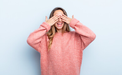 pretty caucasian woman smiling and feeling happy, covering eyes with both hands and waiting for...