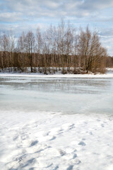 Lake with surface covered with melting snow and small island with bare trees in the distance,  early spring landscape