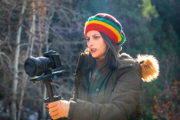 Young woman in rasta hat photographing outdoors with steadicam