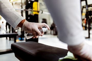 Sportsman disinfecting sports equipment in the gym for safety after COVID-19 pandemic. Disinfecting exercise equipment. Hygiene in gym. Staff cleaning exercise machine in the gym.