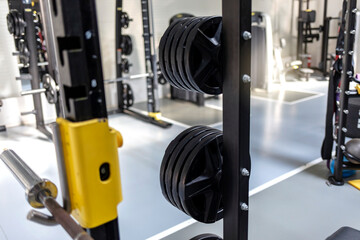 Fototapeta na wymiar Barbells of different weights on the rack. Gym equipment. Sports equipment in the gym. Barbell plates holder rack in the gym. Heavy barbell plates hanging on a rack inside an empty gym.