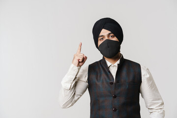 South asian man wearing turban and face mask pointing finger upward