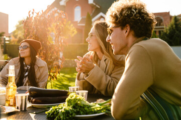 Multiracial friends talking and laughing during barbeque in garden