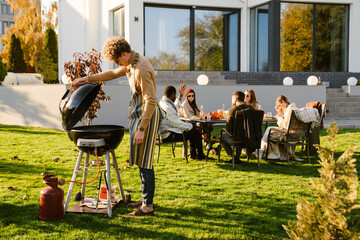 Multiracial friends talking and laughing during barbeque in garden - obrazy, fototapety, plakaty