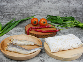 salted fish, raw tempeh and vegetables on a wooden cutting board