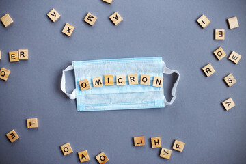 word omicron made by wooden blocks with medical mask on gray background.