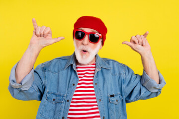 Portrait of attractive funny grey-haired man dancing showing horn sign having fun isolated over bright yellow color background