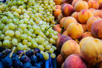 White ripe fresh grapes on a shop counter near blue grapes, peaches