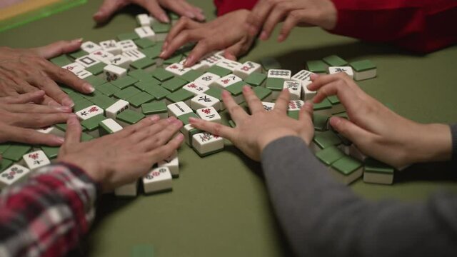 closeup shot of hands mixing green white mahjong piece on the table. people playing tile game together during chinese new year holiday