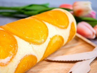 Close up of orange cake roll with slice orange fruit on wooden plate.