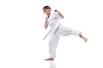Full-length portrait of little boy, karateka in white kimono training isolated over white background