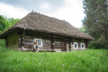 Fototapeta na wymiar In summer, a girl in an authentic Ukrainian national costume poses against the backdrop of a hut in the Pirogovo Museum.