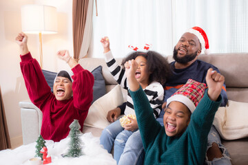 Happiness African family watching movie with excited and fun in the living room for leisure with comfort at home on Christmas day, dad and mom and daughter cheering watching tv with victory.