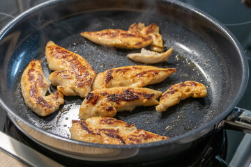 Woman cooking and frying chicken breasts and chicken filet in a pan on an hot stove in the kitchen as delicious meal and diet dinner cuisine for healthy nutrition with smoking hot meat and barbecue