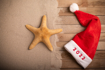 New Year 2022 written on a Santa Claus hat on sandy beach.