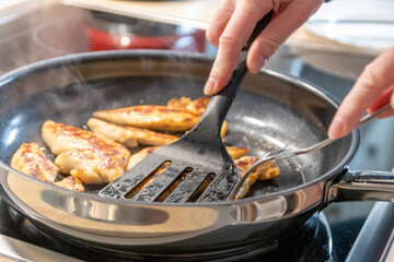 Woman cooking and frying chicken breasts and chicken filet in a pan on an hot stove in the kitchen as delicious meal and diet dinner cuisine for healthy nutrition with smoking hot meat and barbecue