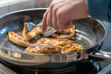 Woman cooking and frying chicken breasts and chicken filet in a pan on an hot stove in the kitchen as delicious meal and diet dinner cuisine for healthy nutrition with smoking hot meat and barbecue