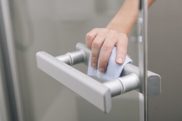 Cleaning glass door handles with an antiseptic wet wipe. Woman hand using towel for cleaning home room door link. Sanitize surfaces prevention in hospital and public spaces against corona virus