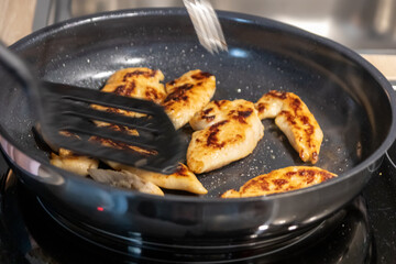 Woman cooking and frying chicken breasts and chicken filet in a pan on an hot stove in the kitchen as delicious meal and diet dinner cuisine for healthy nutrition with smoking hot meat and barbecue