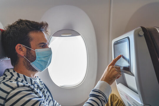 Passenger in medical mask touching inflight entertainment screen