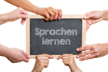 Viele Hände halten Tafel mit Schriftzug „Sprachen lernen“