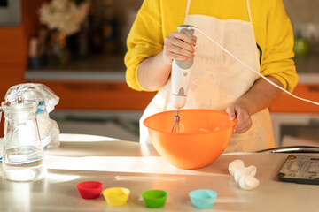 Girl in an apron prepares cupcakes in the kitchen.  girl whipping dough for cupcakes with a blender