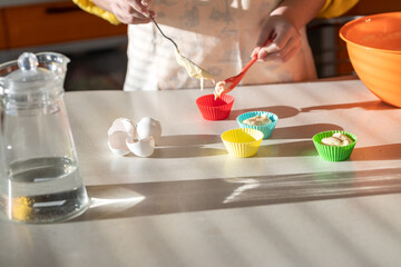 Obraz na płótnie Canvas Girl in an apron prepares cupcakes in the kitchen. person preparing food in kitchen. 