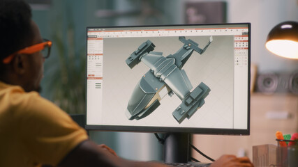 Black man using computer and creating 3D model of futuristic aircraft for videogame or movie while...