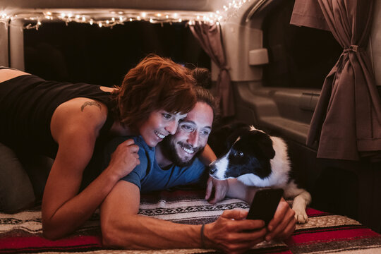 Happy mid adult couple using smart phone with dog in van
