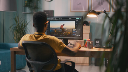 Back view of African American man using software on computer to create visual effects on video with...