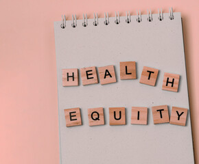 Message health equity with wooden letters on notebook in pink.