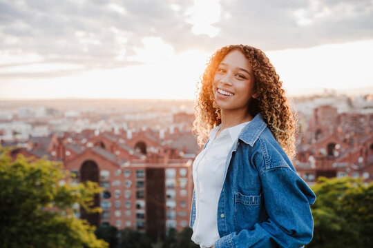 Smiling woman wearing denim jacket by city during sunset