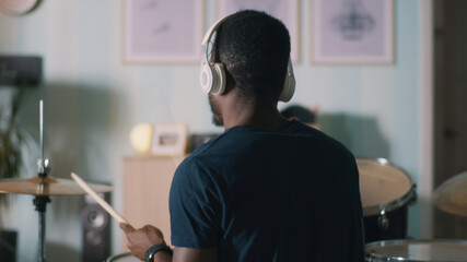Back view of African American musician in headphones playing drums during rehearsal at home in...