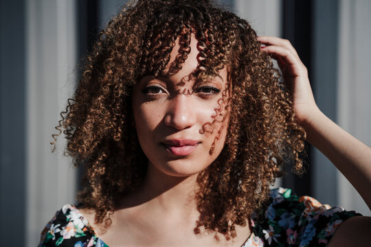 Young curly haired woman standing with hand in hair during sunny day