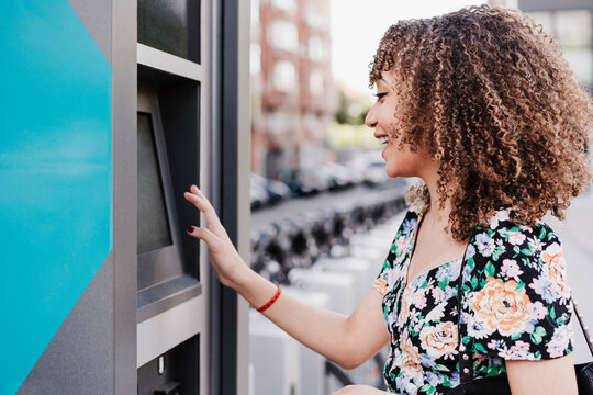 Cheerful young woman with curly hair payment machine for bicycle sharing system