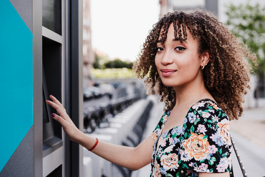 Young woman with curly hair payment machine for bicycle sharing system