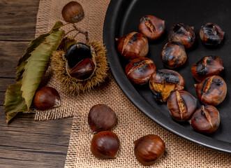 Roasted chestnuts and chestnuts, one of which with hedgehog , on a baking tray and on a wooden table