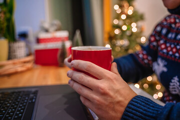 A man in a festive sweater drinks cocoa with marshmallows during the New Year holidays and Christmas. Beautiful atmosphere of holidays at home and in the workplace