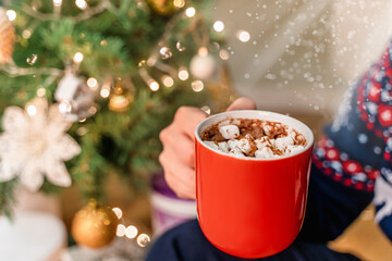A man in a festive sweater drinks cocoa with marshmallows during the New Year holidays and...