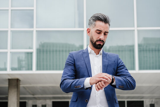 Businessman checking time on wristwatch in front of building